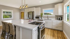 A modern kitchen with a central island, stainless steel appliances, and a view of the outdoors. - Poipu Beach Cottage AC, 1 BR, Sleeps 4 (Koloa)