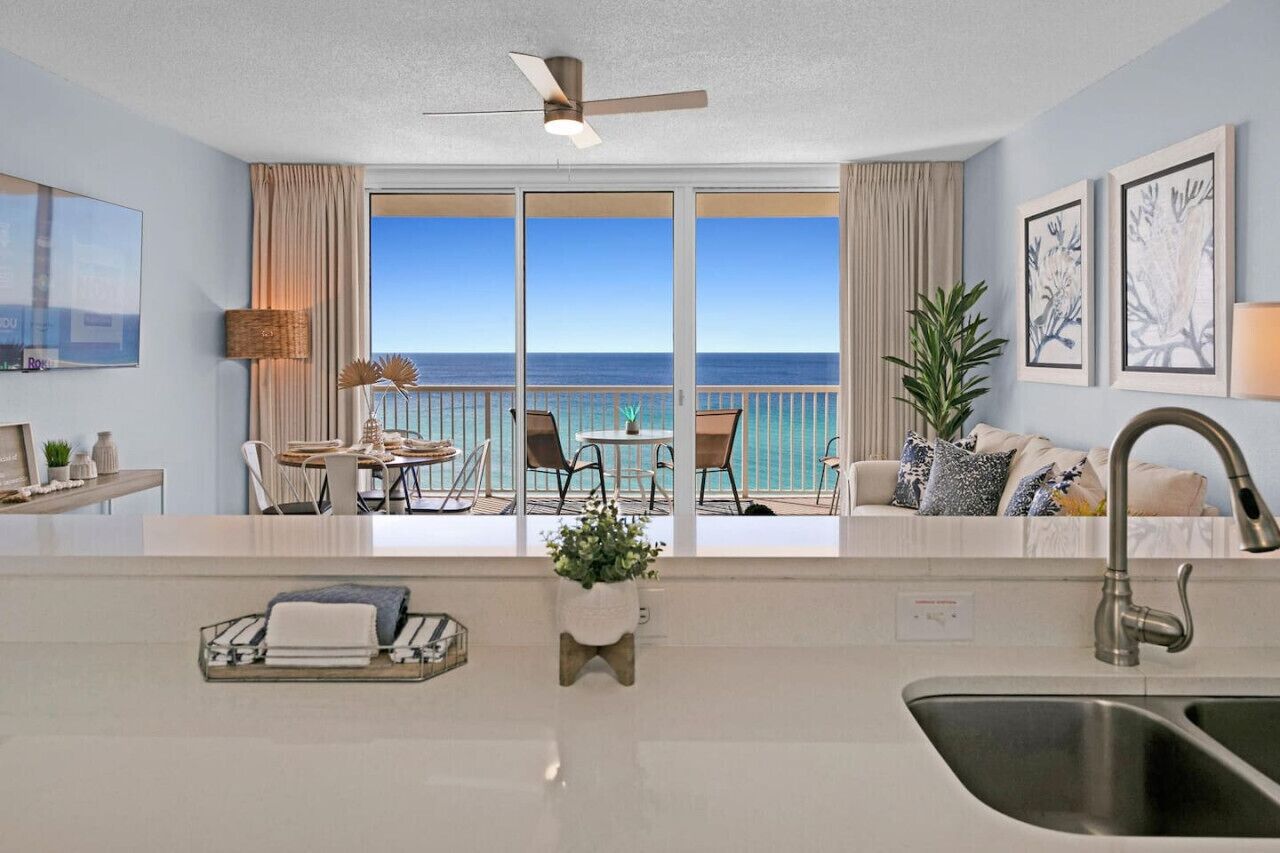 A modern hotel room with a balcony, a dining area, and a kitchen with a sink.