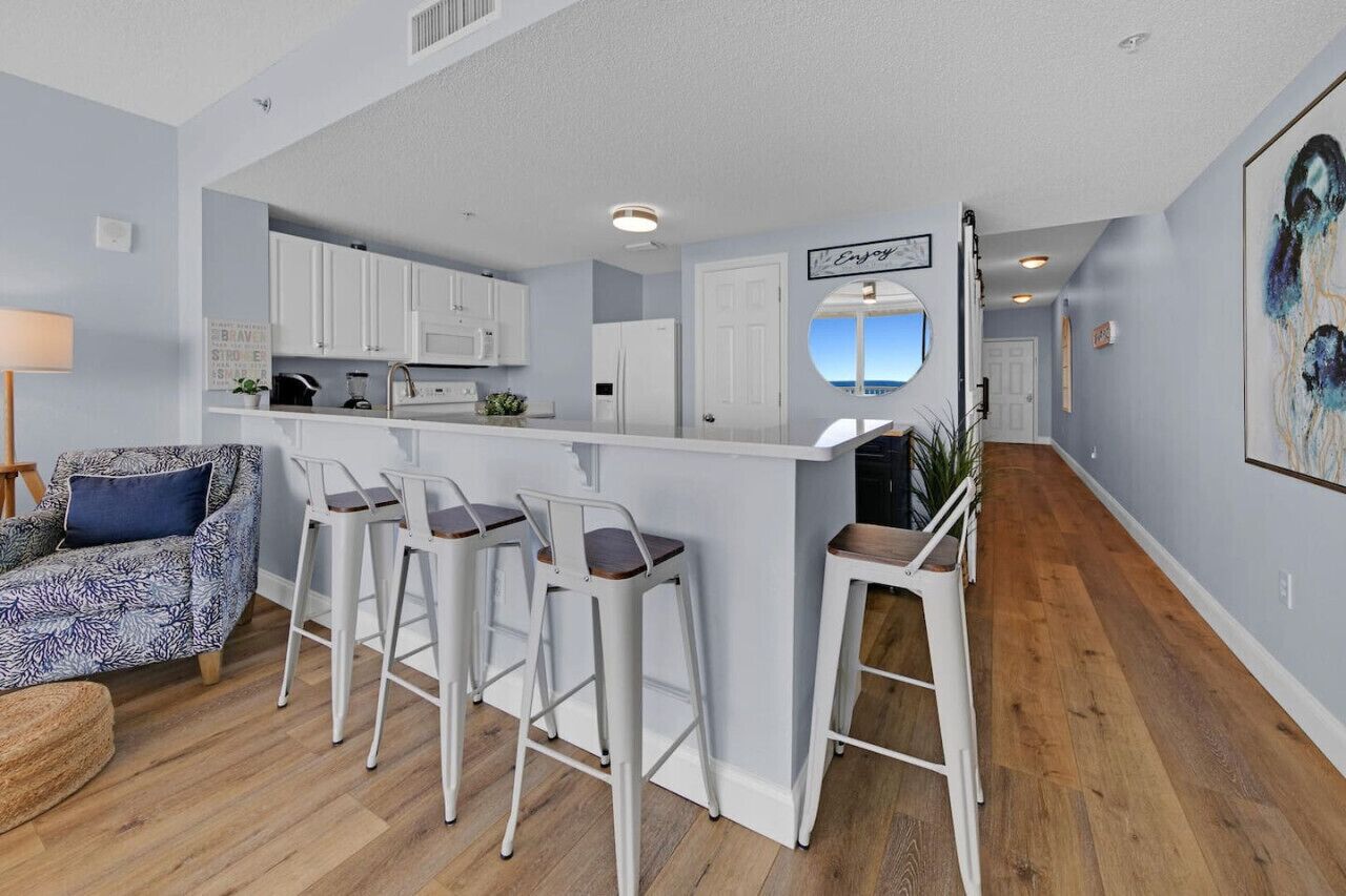 A modern kitchen with white cabinets, a bar area with stools, and a view of the ocean through a window.