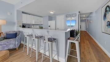 A modern kitchen with white cabinets, a bar area with stools, and a view of the ocean through a window.
