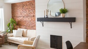 Ein Wohnzimmer mit Backsteinwand, einem weißen Sofa, einem schwarzen Sessel, einem Tisch und einem Kamin mit Spiegel und Kerzen.