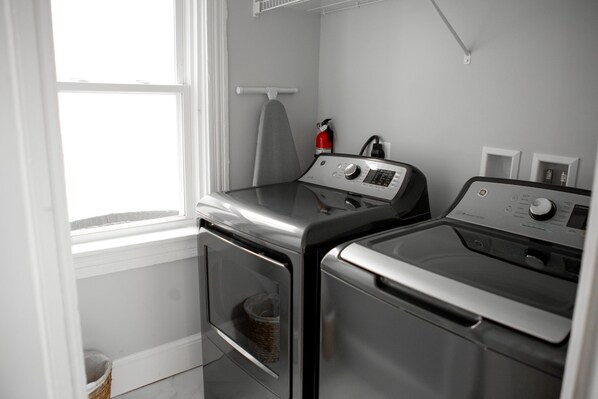 A laundry room with two stainless steel washers and dryers, a fire extinguisher, and a window.