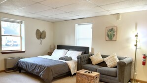 Een slaapkamer met een bed, een grijze bank, een rieten mand en een schilderij van een cactus.