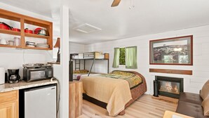 A compact room with a kitchenette, a bed, a fireplace, and a window with a view. - Pet friendly Fun Family Cabin- 3 Beds, Fireplace, Horseshoes, Swing, Hottub (Payson)
