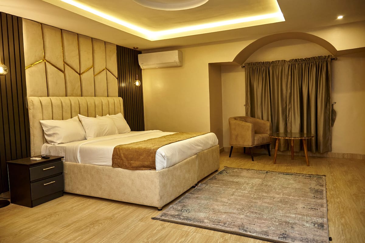 A modern bedroom with a large bed, a bedside table, an arched window with curtains, and a small round table.
