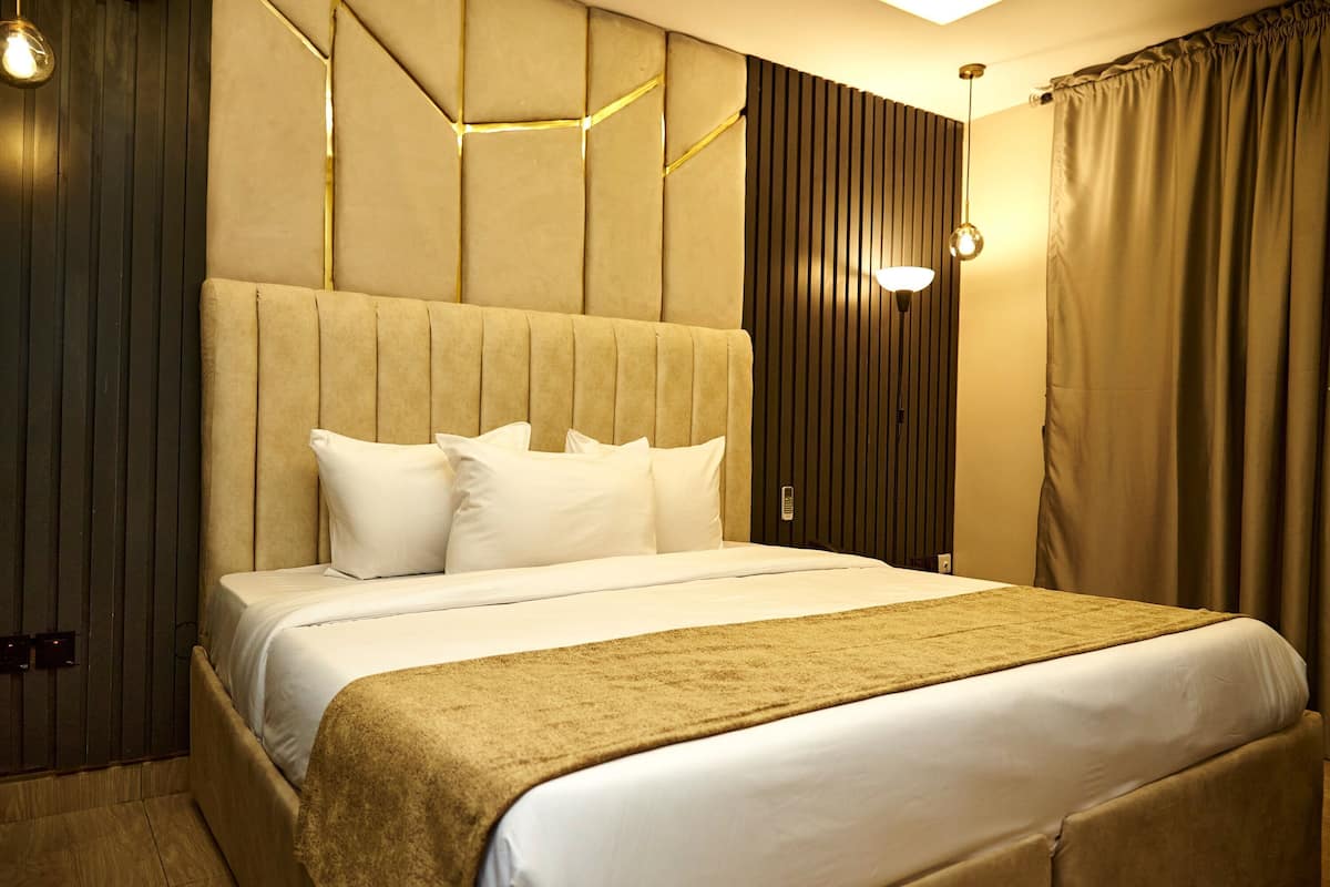 A hotel room with a large bed, a headboard, a wall-mounted light fixture, and a curtain.
