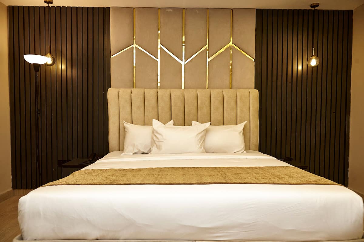 A modern hotel room with a large bed, a wooden headboard, and two wall-mounted lights.