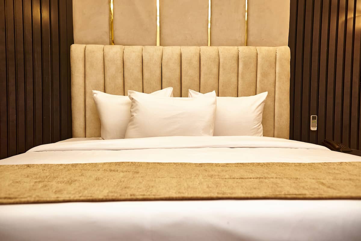 A bed with a beige headboard, white pillows, and a beige throw blanket.