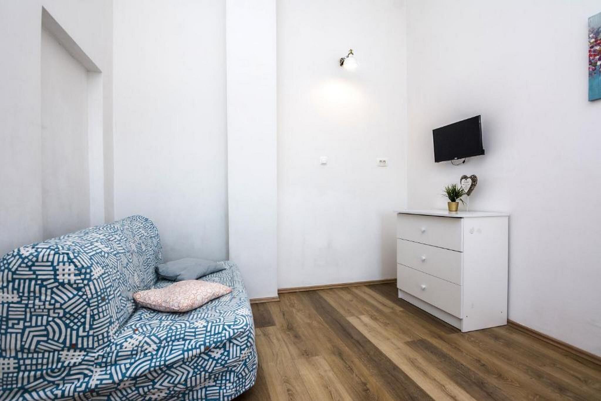 Une petite pièce moderne, avec un canapé à motifs, une commode blanche et un téléviseur fixé au mur.