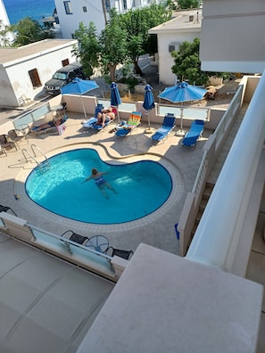 Relax by the pool surrounded by comfortable lounge chairs and umbrellas, with a balcony offering a view of the surrounding neighborhood and water.