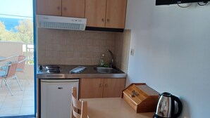 Een compacte keuken met houten kastjes, een inbouwoven, een spoelbak en een kleine koelkast. Er staat een eettafel met stoelen en een waterkoker op.
