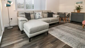 Una sala de estar moderna con un sofá seccional, una mesa de comedor con sillas, un aparador gris y una lámpara de pie.