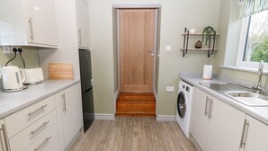 Cocina compacta con armarios blancos, una puerta de madera, lavadora y una encimera con tetera y tostadora.