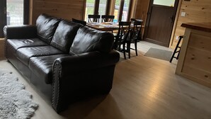 L’intérieur chaleureux d’un chalet avec un canapé en cuir, une table à manger en bois, des chaises et un lustre.