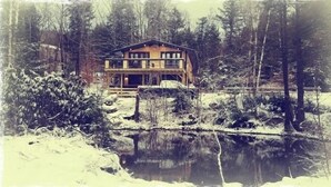 Une cabane en bois dotée d’un balcon, entourée d’un paysage enneigé et bordée par une étendue d’eau.