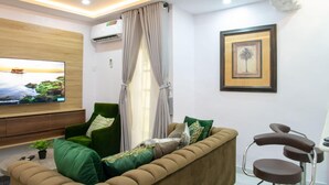 Un salon moderne avec un canapé, un fauteuil vert, un téléviseur et un tableau encadré accroché au mur.