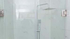 Une cabine de douche fermée par des parois en verre, dotée d’un pommeau de douche à main et d’un robinet fixé au mur.