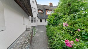 Ein schmaler Gang mit einem weißen Gebäude auf der einen Seite und einem Garten mit rosa Blumen auf der anderen.