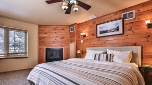 Une chambre à coucher avec un grand lit, des murs en bois, une cheminée et un ventilateur de plafond.