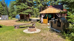 Un espace extérieur rustique, agrémenté d’une structure en bois, d’un foyer en pierre et d’un coin barbecue.