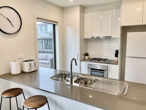 A modern kitchen with a built-in sink, a gas stove, a refrigerator, and two bar stools. - Holiday on Dromana by Ready Set Stay- 150m from the beach (Safety Beach)