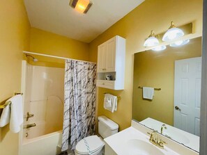 Een badkamer met bad, toilet en wastafel. Handdoeken hangen aan de muur en er is een douchegordijn.