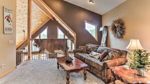 A cozy living room with a high ceiling, a large window, and a rustic decor. - Spacious Lead Getaway w/ Private Hot Tub & Deck! (Lead)