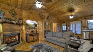 A cozy cabin interior with a fireplace, leather furniture, a television, and wooden walls. - Overlook Oasis - Hot tub, firepit, and comfy king beds! (Blue Ridge)