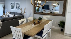 A dining area with a wooden table, white chairs, and a chandelier. - NEWLY RENOVATED Oceanside Oasis at Kawama Tower (Key Largo)
