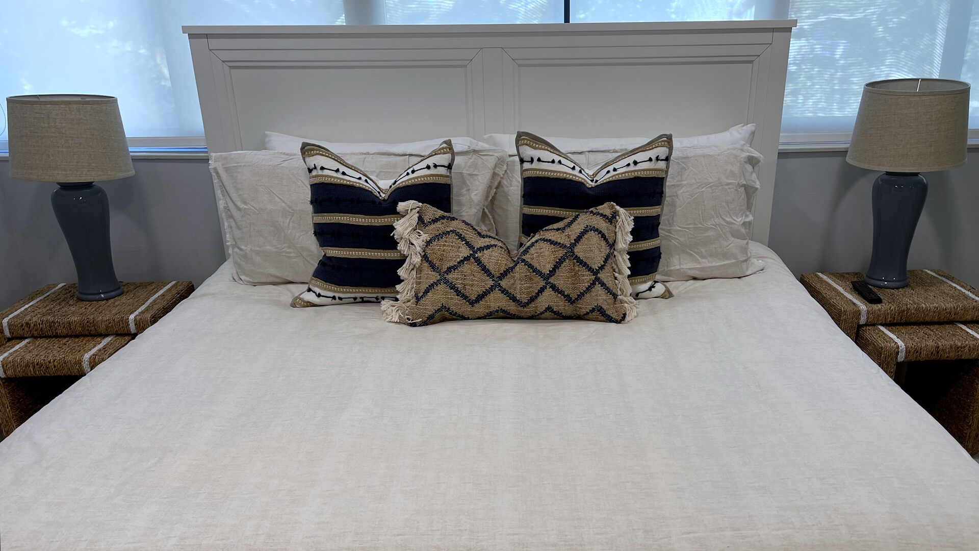 Una cama con sábanas blancas, dos mesitas de noche con lámparas y almohadones decorativos.