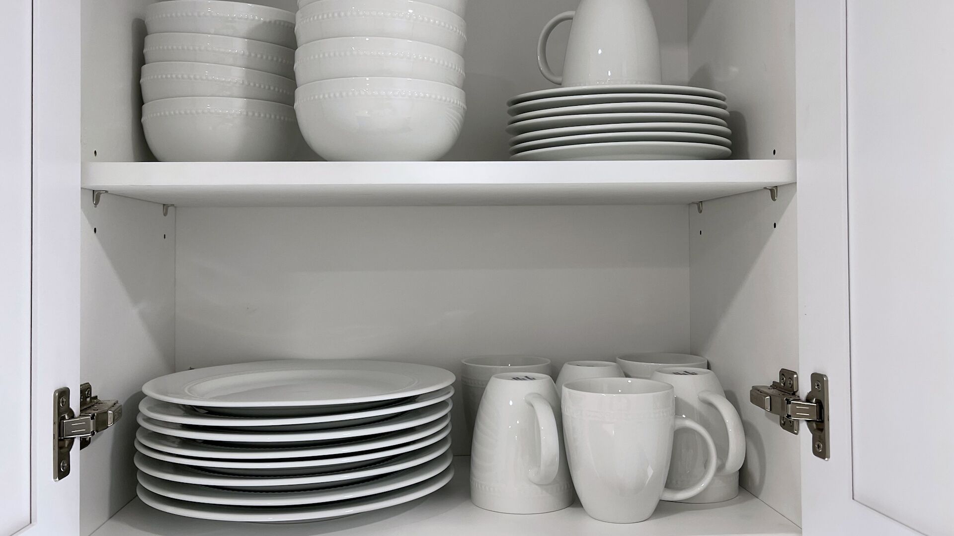 Un meuble blanc, doté d’étagères où sont rangées des assiettes, des bols et des tasses blancs.