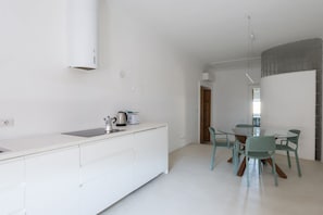 A modern kitchen with white cabinetry, a dining area with teal chairs, and a visible door leading to another room.