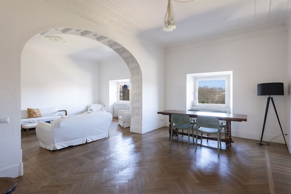A room with a dining table, chairs, a sofa, and a lamp.
