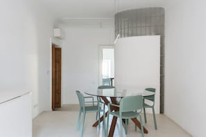 A modern dining area with a glass table and matching chairs, a whiteboard, and a wooden door.