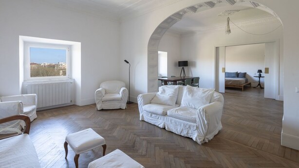 Un salon spacieux doté d’un parquet en point de Hongrie, de meubles blancs, d’une grande fenêtre et d’un plafond en arc de cercle.