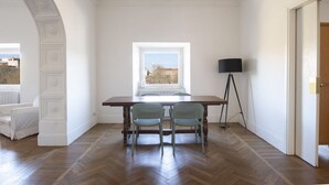 Une pièce dotée d’un parquet en bois disposé en chevrons, d’un mur blanc, d’une fenêtre offrant une vue, d’un lampadaire et d’une table avec deux chaises.