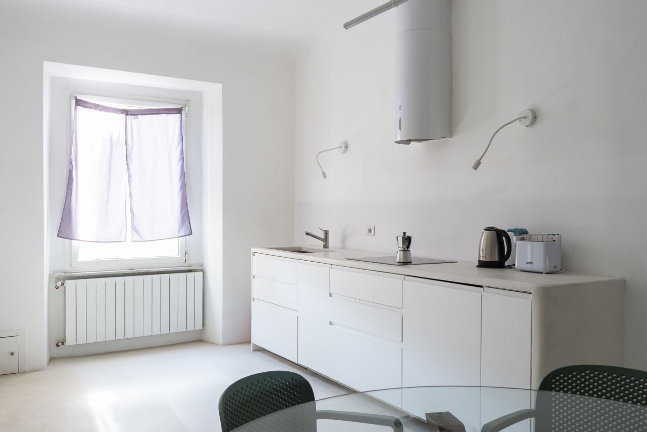 A modern kitchen with a window, white cabinets, and a kettle on the counter.