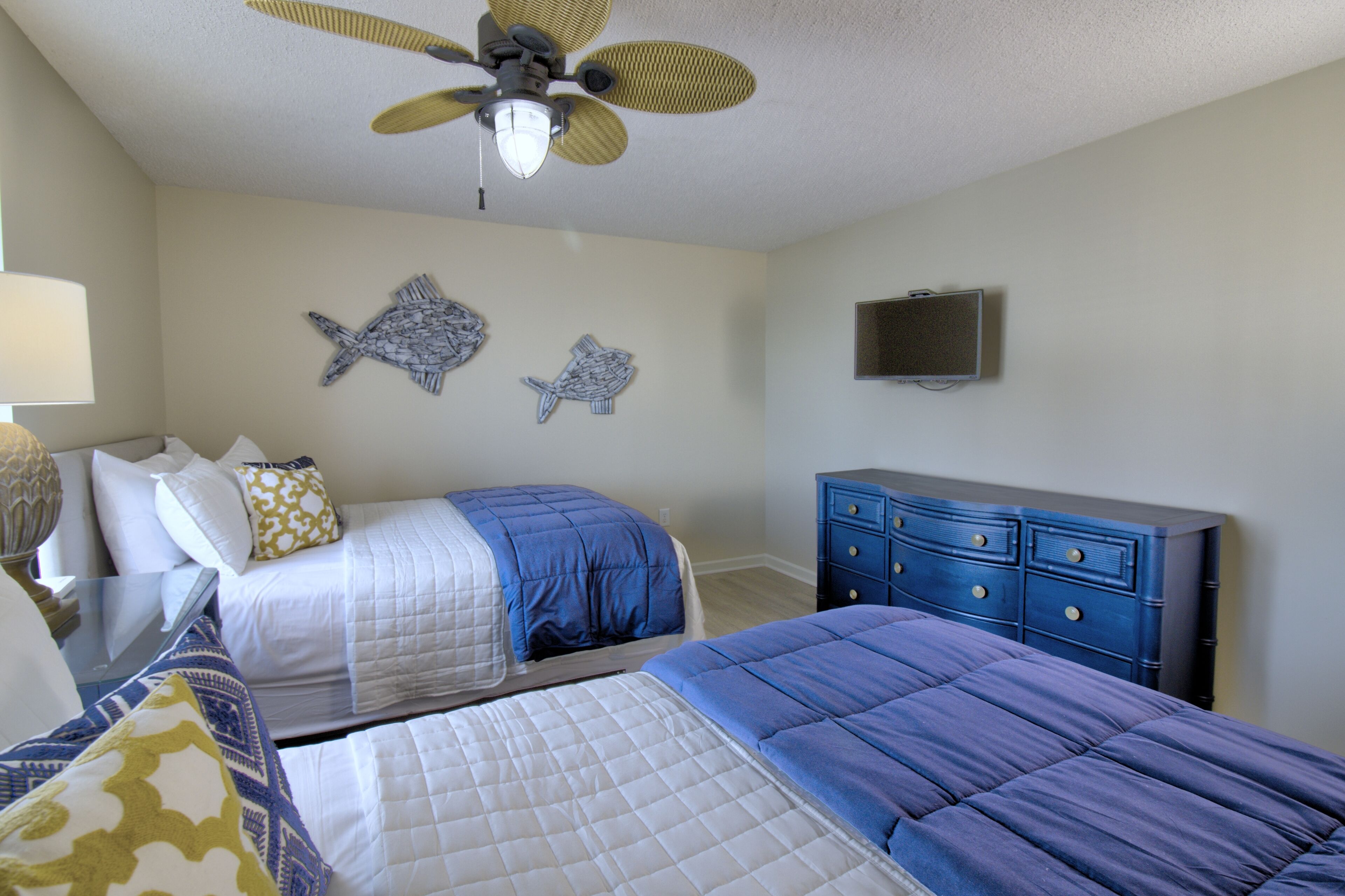 A bedroom with two beds, a ceiling fan, a dresser, and wall art.