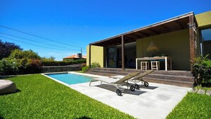 A modern house with a swimming pool, a covered patio, and a well-maintained lawn.