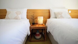 A hotel room with two beds, each with white bedding and decorative pillows. There is a wooden nightstand between the beds with a lamp and a woven basket.