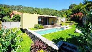 A modern house with a swimming pool, a patio, and a view of a forested hill.
