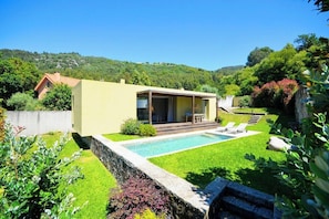 Una casa moderna con piscina, patio y vistas a una colina boscosa.