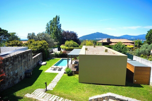 Un espacio exterior moderno con piscina, muros de piedra y vistas a montañas distantes.