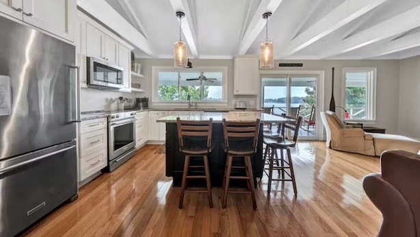 Una cocina moderna con electrodomésticos de acero inoxidable, taburetes de madera y una isla grande.