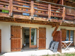 A wooden building with a balcony, open doors leading to a room, and a table outside.