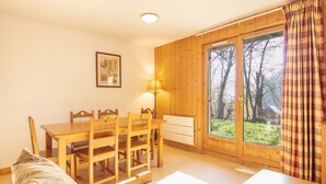 A cozy room with a wooden dining table and chairs, a bed with a plaid bedspread, a window with curtains, and a framed picture on the wall. - Cosy apt 4/6 ppl, terrace, heated pool (Saint-Sorlin-d´Arves)