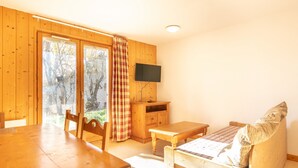 A wooden interior with a dining table, a sofa, a TV mounted on the wall, and a view through a glass door. - Cosy apt 4/6 ppl, terrace, heated pool (Saint-Sorlin-d´Arves)