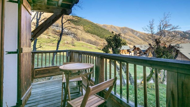 Une terrasse en bois avec une table et des chaises, offrant une vue sur un paysage montagneux parsemé de maisons.