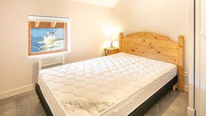 Ein Schlafzimmer mit Holz-Kopfteil, einem Fenster mit Blick auf ein Haus, einem Nachttisch mit Lampe und einer Matratze.