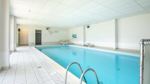 Ein sauberer, überdachter Pool mit klarem, blauem Wasser, gefliesten Wänden und einem Fliesboden. Zwei Metallleiter und einige Liegestühle befinden sich am Poolrand.